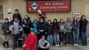 Middle school students stand together to pose for a group shot in front of their school sign